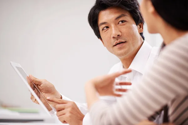 Analizando la información juntos. Disparo de dos colegas de negocios asiáticos sentados con una tableta digital y discutiendo trabajo. — Foto de Stock