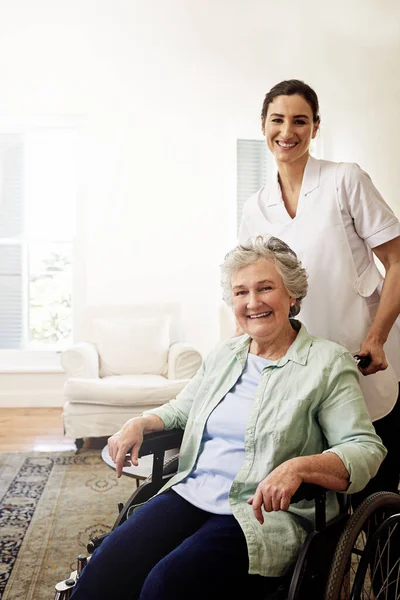 Sei in buone mani con lei. Ritratto di una badante sorridente e di una donna anziana in sedia a rotelle a casa. — Foto Stock