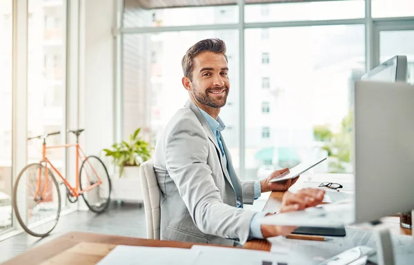 Multitasking mijn weg naar succes. Portret van een knappe jonge zakenman aan het werk op een laptop en digitale tablet in een kantoor. — Stockfoto