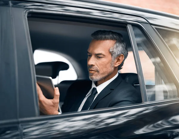 保持联系是成功的关键。上午上下班时坐在汽车后座上用平板电脑拍摄的一位英俊的成熟商人的合影. — 图库照片