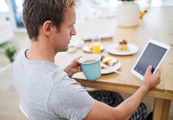 Mi godo la colazione. Colpo di un bell'uomo che usa il suo tablet mentre fa colazione a casa. — Foto Stock