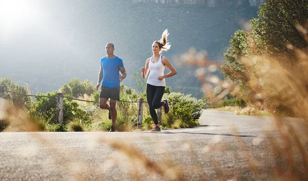Az energia és a kitartás mindent legyőz. Egy sportos párról, akik egy hegyi úton futnak.. — Stock Fotó