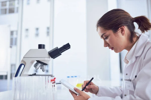 Forschung ist nur ein Teil der Aufgabe. Aufnahme einer fokussierten jungen Wissenschaftlerin, die an einem digitalen Tablet arbeitet, während sie in einem Labor sitzt. — Stockfoto