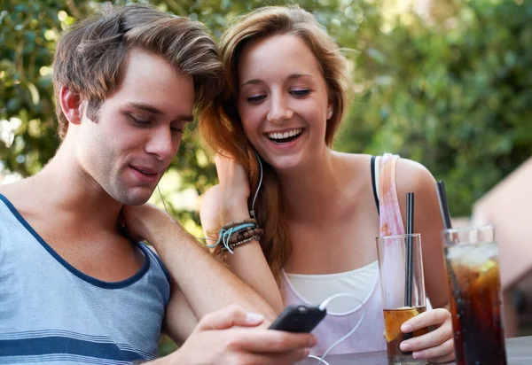 Socializzare nel ventunesimo secolo. Graziosa coppia di adolescenti che condividono un lettore MP3 e ascoltano musica mentre si godono le loro bevande. — Foto Stock