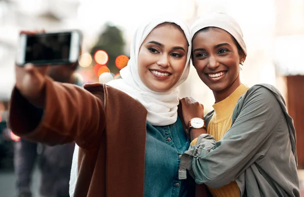 Hora da selfie. Tiro recortado de duas jovens mulheres atraentes que estão juntas e vestindo lenços de cabeça ao tirar uma selfie com seu celular. — Fotografia de Stock