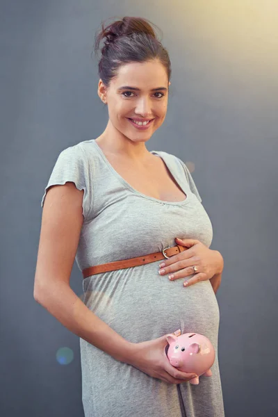 Saving up for baby. Cropped shot of a pregnant woman holding a piggybank against a gray background. — Stock Photo, Image