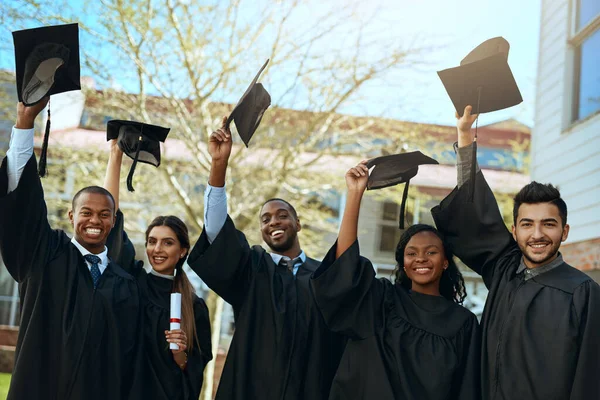 Utbildning för segern. Porträtt av en grupp glada unga studenter som tar av sig hatten på examensdagen. — Stockfoto