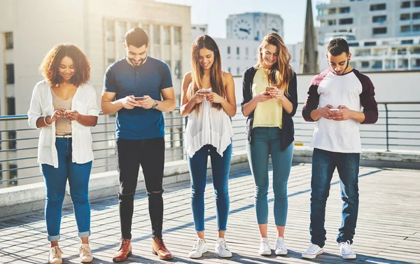 Ansluten i staden. Fullständig bild av en grupp ungdomar som sms:ar på sina mobiler när de står utomhus. — Stockfoto