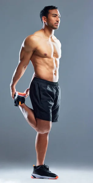 Devi guadagnartelo. Studio shot di un giovane muscoloso che distende le gambe su uno sfondo grigio. — Foto Stock