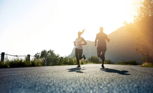 Theres one way to succeed and thats to give everything. Low angle shot of two people running on a tarmac road. — Stock Photo, Image