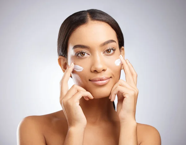 La migliore crema dissetante per la pelle. Studio shot di una giovane donna attraente che applica idratante al suo viso su uno sfondo grigio. — Foto Stock