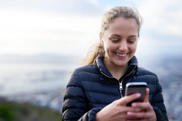 Mantenerse en contacto dondequiera que vaya. Cortada la foto de una joven atractiva enviando mensajes de texto en un teléfono celular fuera. —  Fotos de Stock