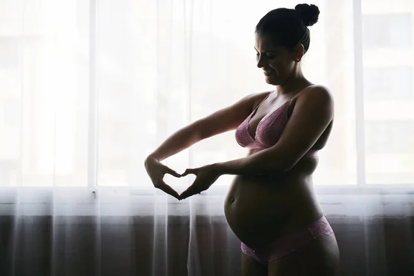 Seu coração está crescendo junto com seu bebê. Tiro cortado de uma jovem mulher grávida atraente em pé em seu quarto em casa. — Fotografia de Stock