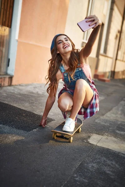 Többfunkciós a korcsolyás módszer. Lelőttek egy gondtalan fiatal nőt, aki alacsonyan ül a gördeszkán, miközben napközben önarcképet készített a mobiljával.. — Stock Fotó