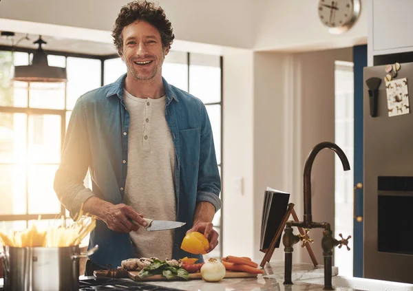 Cocinar es un poco como la magia. Retrato de un soltero feliz cortando verduras en su cocina. —  Fotos de Stock