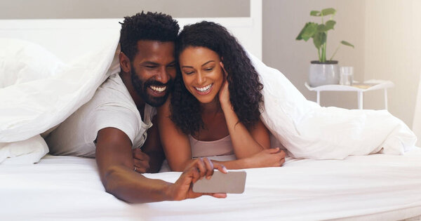 I appreciate everyday with you, lets take a selfie. Cropped shot of a young attractive couple taking a selfie in bed at home.