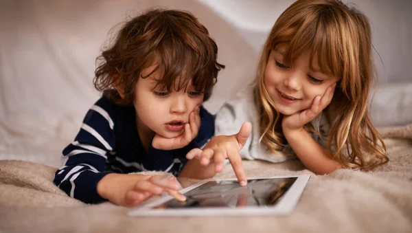Los juegos de mesa se vuelven digitales. Tiro de dos adorables hermanos usando una tableta digital mientras están acostados en una cama. —  Fotos de Stock
