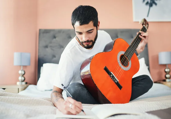 Tenho a certeza que isto vai ser um sucesso. Tiro de um homem escrevendo em seu caderno enquanto tocava guitarra em casa. — Fotografia de Stock