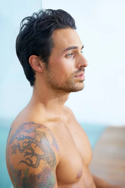 Perfil da perfeição masculina. Perfil de um jovem bonito com tatuagens sentado de costas contra um painel de vidro. — Fotografia de Stock