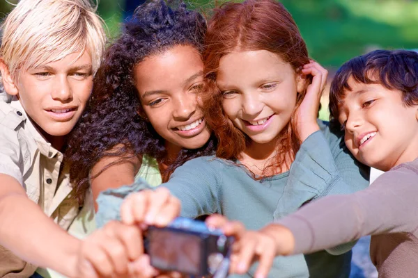 Capturando momentos de verano infantil. Un grupo de niños mirando una cámara digital mientras están sentados afuera. —  Fotos de Stock