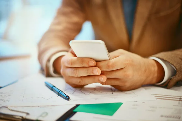 Kommunikation ist das Geheimnis seines Erfolgs. Hochwinkelaufnahme eines unkenntlichen männlichen Designers, der eine SMS von seinem Schreibtisch im Büro verschickt. — Stockfoto