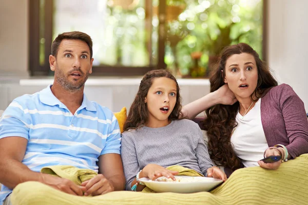 Assolutamente scioccato. Girato di una famiglia seduta sul divano del loro salotto a guardare un film e mangiare popcorn. — Foto Stock