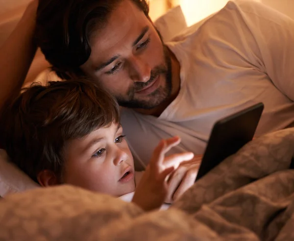 Ώρα για ψηφιακή ιστορία. Πατέρας και γιος ξαπλωμένοι στο κρεβάτι με ένα e-reader. — Φωτογραφία Αρχείου