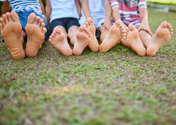 I tuoi piedi ti porteranno dove il divertimento è. Colpo ritagliato di un gruppo di bambini seduti a piedi nudi sull'erba. — Foto Stock
