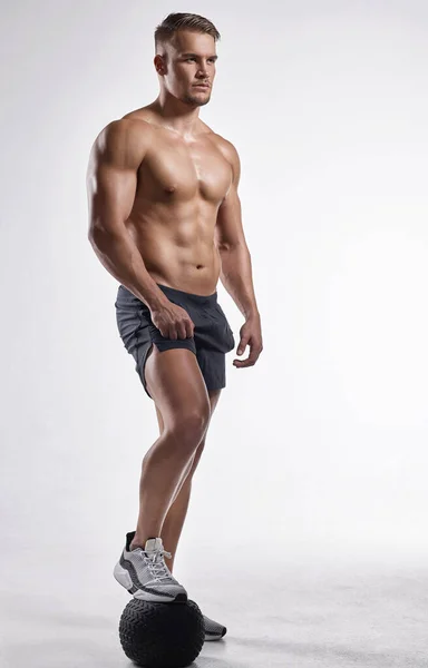 Si tienes tiempo libre, gástalo en el gimnasio. Estudio de un hombre musculoso de pie con el pie en una pelota de ejercicio. —  Fotos de Stock