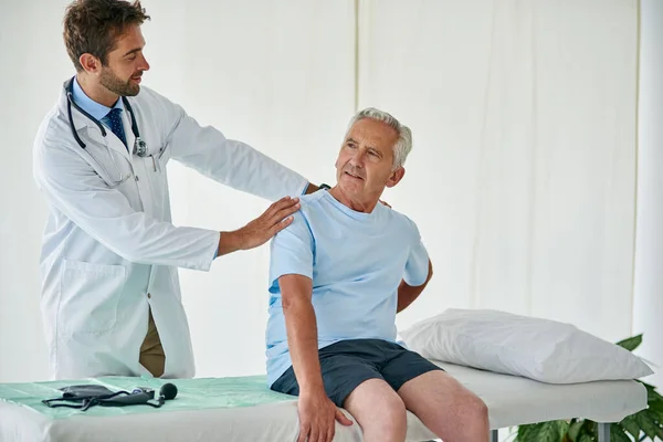 The pain is worse on that side. Cropped shot of a young male doctor examining a senior patient with back pain in his office. — Stock Photo, Image