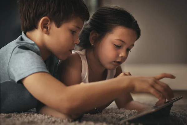 Le divertissement amical des enfants est juste une application loin. Tourné d'un frère et d'une sœur adorables à l'aide d'une tablette numérique ensemble sur le sol à la maison. — Photo