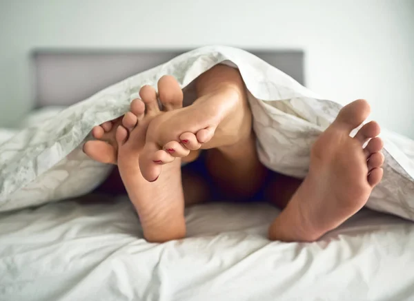 轻快的脚被一对夫妇的脚从床单底下探出头射中. — 图库照片