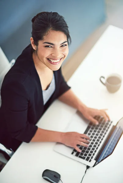 Ik heb een geweldige dag. Hoge hoek portret van een aantrekkelijke jonge zakenvrouw werken op een laptop in haar kantoor. — Stockfoto