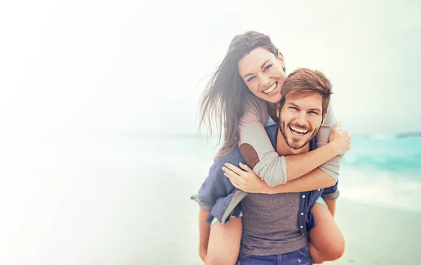 Stranddejt. Beskuren bild av en ung man ge sin flickvän en piggyback rida på stranden. — Stockfoto