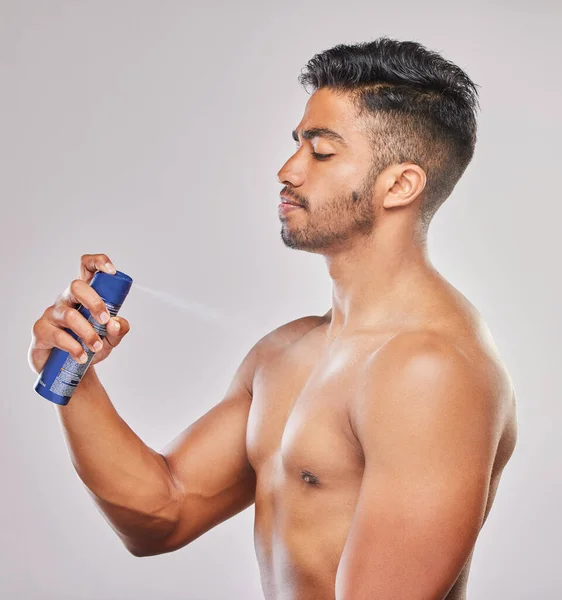 We moeten alle hoeken bekijken. Schot van een jongeman die deodorant tegen een grijze achtergrond aanbrengt. — Stockfoto