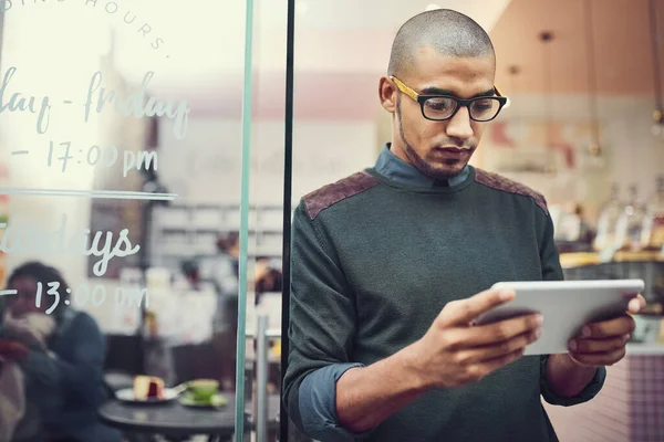 Mantener un ojo en su competencia. Fotografía de un hombre usando su tableta digital mientras estaba de pie en la entrada de un café. —  Fotos de Stock