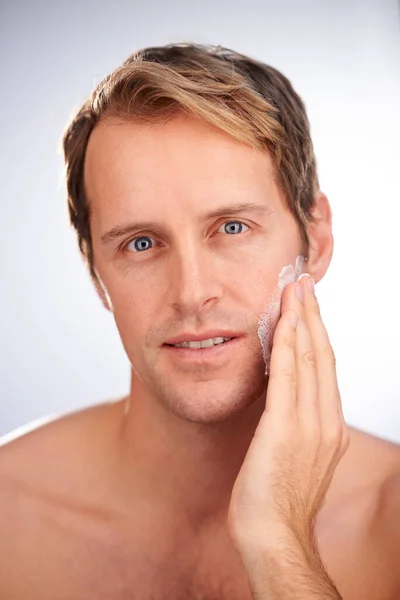 Hladká holení a měkká pokožka. Studio záběr pohledného muže, který aplikuje zvlhčovač. — Stock fotografie