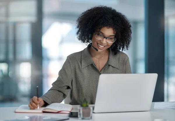 Multitasking al massimo. Girato di una giovane agente donna che sorride mentre prende appunti mentre lavora in un call center. — Foto Stock