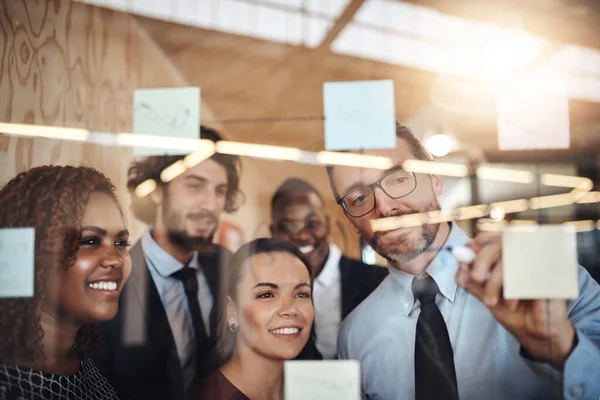 Deras vision kommer till liv. Skjuten av en grupp affärsmän brainstorming med anteckningar på en glasvägg i ett kontor. — Stockfoto
