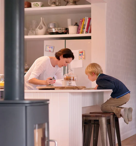 Mira lo que haces, mami. Shot de un lindo niño viendo a su madre trabajar en su cocina en casa. — Foto de Stock