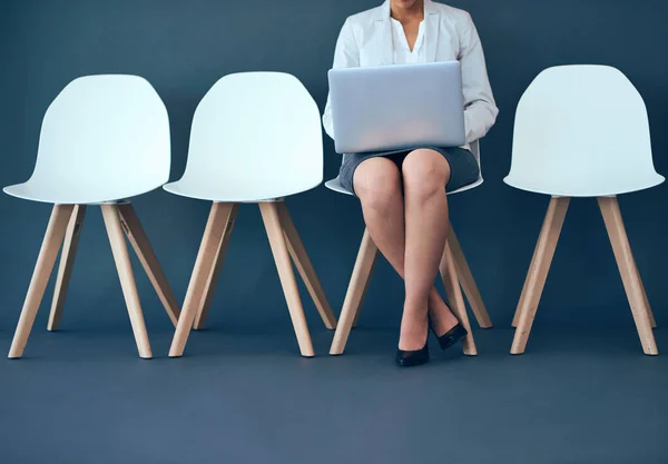 Doe wat zaken terwijl je wacht. Studio shot van een onherkenbare zakelijke vrouw met behulp van een laptop tijdens het wachten in de rij tegen een grijze achtergrond. — Stockfoto