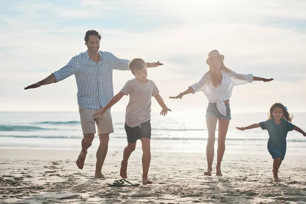 Είναι ένας αγώνας. Full length πλάνο ενός ευτυχισμένου νεαρού ζευγαριού που απολαμβάνει μια παιχνιδιάρικη μέρα με τα δύο παιδιά του στην παραλία. — Φωτογραφία Αρχείου