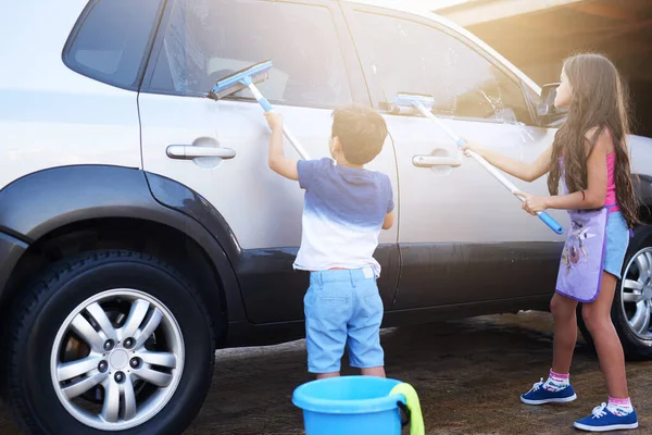 Limpiar es responsabilidad de todos. Un disparo de un niño pequeño y su hermana lavando un coche en casa. — Foto de Stock