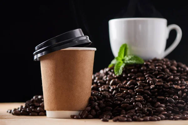 Hoeveel kopjes drink je per dag. Close-up shot van een papieren beker op een oppervlak, met een theekopje en muntblad rustend op een stapel koffiebonen op de achtergrond. — Stockfoto