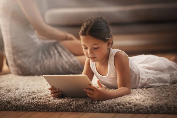 Beaucoup à apprendre sur le World Wide Web. Prise de vue d'une adorable petite fille utilisant une tablette numérique sur le sol à la maison avec sa mère en arrière-plan. — Photo