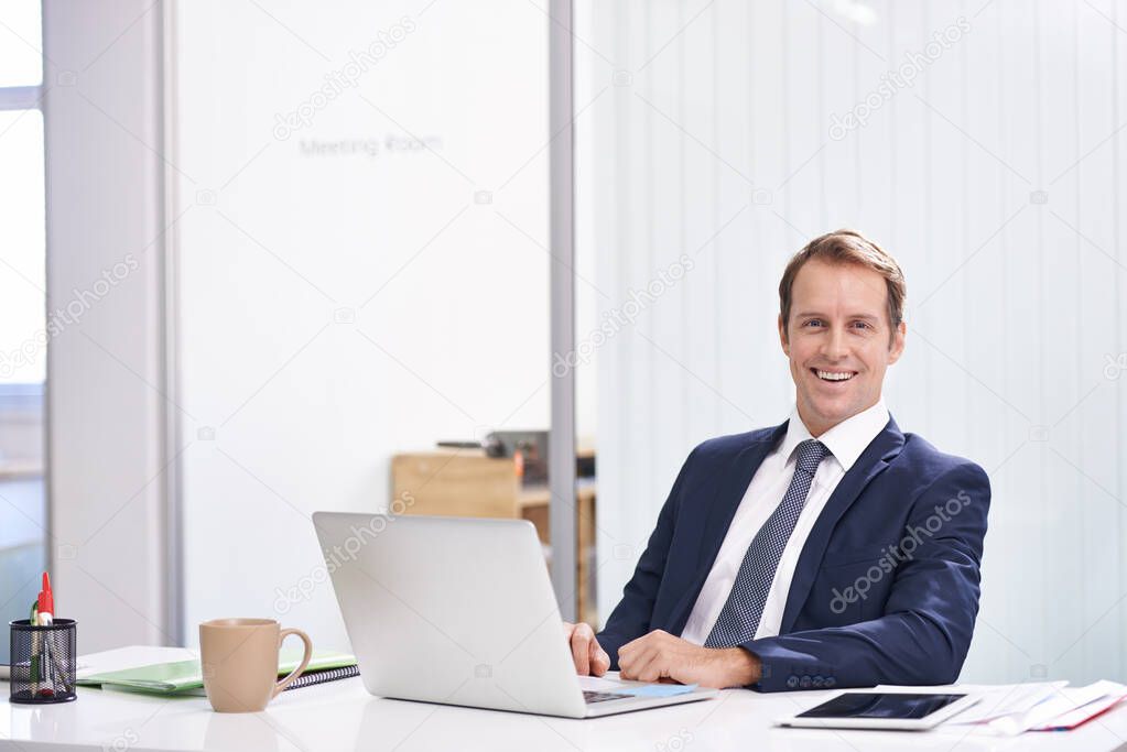 His door is always open. Portrait of a handsome young businessman sitting at his desk with his laptop.
