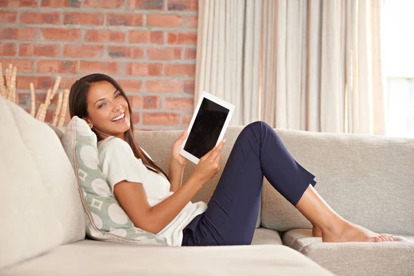 Su tableta digital siempre está cerca. Retrato de una joven atractiva usando una tableta digital mientras está sentada en el sofá. — Foto de Stock