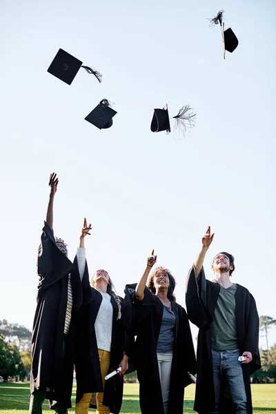 Todas las recompensas valen la pena. Foto de un grupo de estudiantes lanzando sus sombreros al aire en el día de la graduación. —  Fotos de Stock
