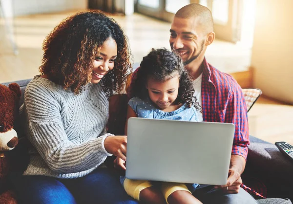 Conectar-se como uma família não é muito difícil com a tecnologia de hoje. Tiro de uma menina adorável e seus pais usando um laptop juntos no sofá em casa. — Fotografia de Stock