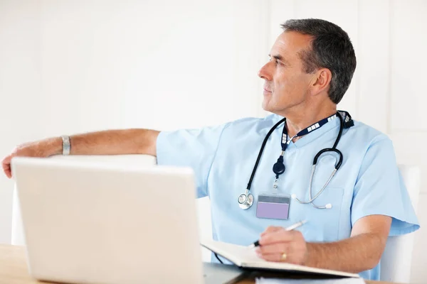 Un dottore anziano che annota il suo programma con un portatile sulla scrivania. Ritratto di un medico anziano che nota il suo programma con laptop sulla scrivania. — Foto Stock